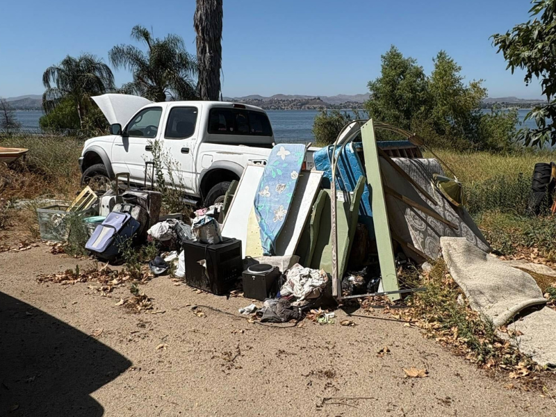 Junk removal Lake Elsinore — mattresses, furniture, trash bags, and wood stacked by a white pickup near the lake, cleared by Corona Junk Removal